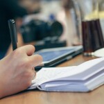 pen and diary in a hand with other things on the table