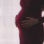 pregnant lady in maroon dress putting her hands on stomach